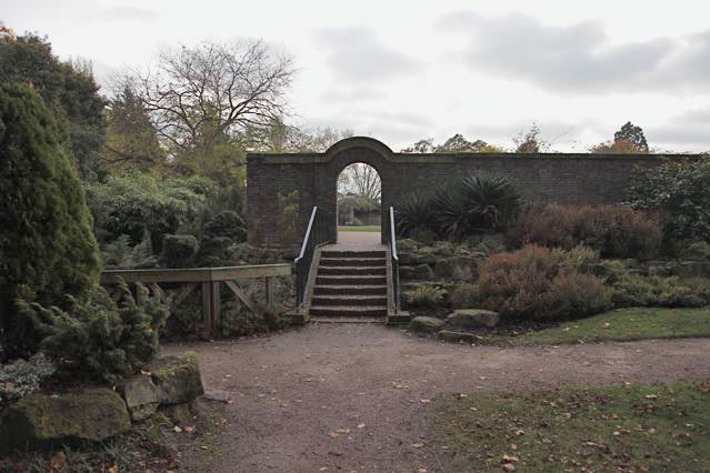 Beautiful historic house garden with an old stone bridge, walled gardens, manicured hedges, a circular pond and an ornate fountain