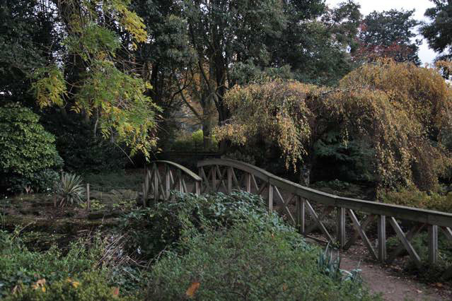 Beautiful historic house garden with an old stone bridge, walled gardens, manicured hedges, a circular pond and an ornate fountain