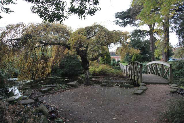 Beautiful historic house garden with an old stone bridge, walled gardens, manicured hedges, a circular pond and an ornate fountain