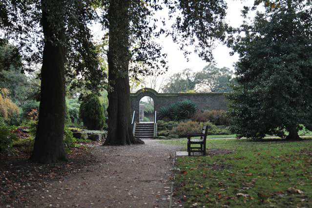 Beautiful historic house garden with an old stone bridge, walled gardens, manicured hedges, a circular pond and an ornate fountain