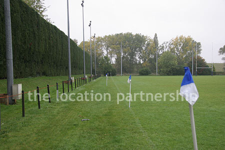 Rugby pitch with very graphic steel stand and huge straight hedge