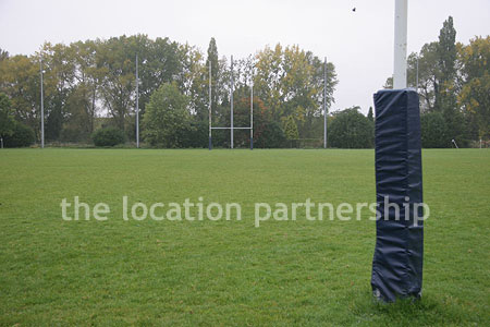 Rugby pitch with very graphic steel stand and huge straight hedge