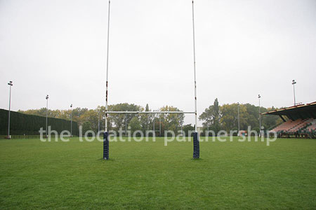 Rugby pitch with very graphic steel stand and huge straight hedge