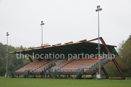 Rugby pitch with very graphic steel stand and huge straight hedge