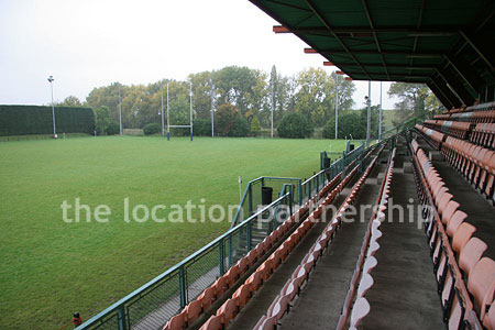 Rugby pitch with very graphic steel stand and huge straight hedge
