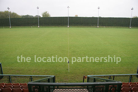 Rugby pitch with very graphic steel stand and huge straight hedge