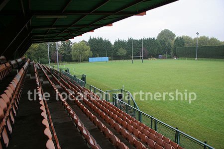 Rugby pitch with very graphic steel stand and huge straight hedge