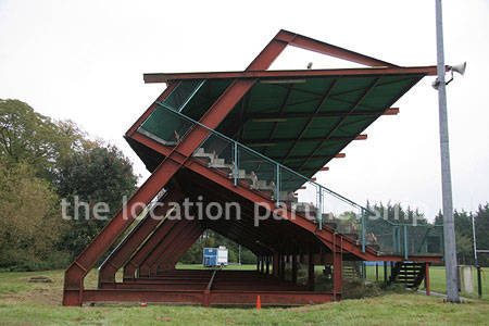 Rugby pitch with very graphic steel stand and huge straight hedge