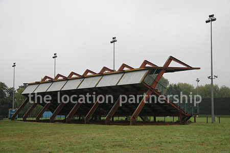 Rugby pitch with very graphic steel stand and huge straight hedge
