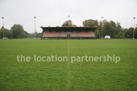 Rugby pitch with very graphic steel stand and huge straight hedge